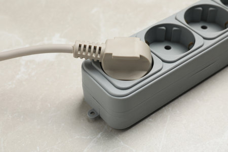 Power strip with extension cord on gray marble table, closeup. Electrician's equipment