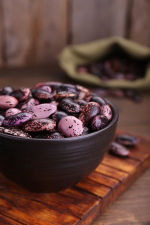 Bowl with dry kidney beans on wooden table, closeup