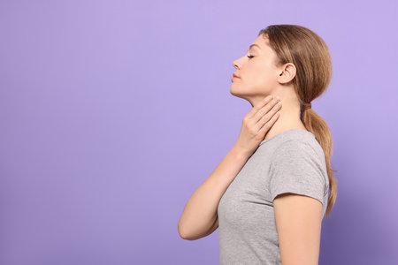 Woman suffering from sore throat on violet background. Space for textの写真素材