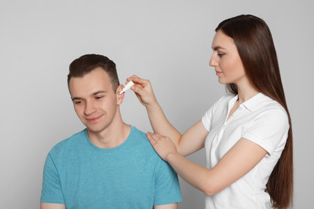 Woman dripping medication into man's ear on light grey backgroundの写真素材