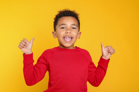 African-American boy showing thumbs up on yellow backgroundの写真素材