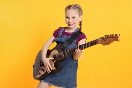 Cute girl with electric guitar on orange backgroundの写真素材