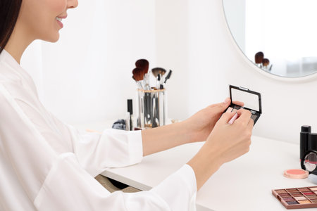 Woman with eyeshadow palette and brush at dressing table, closeupの写真素材