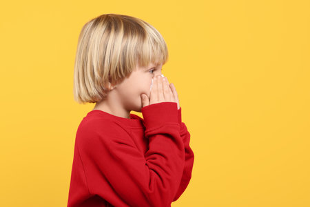 Boy blowing nose in tissue on orange background, space for text. Cold symptomsの写真素材