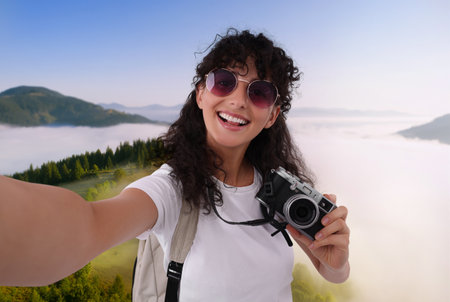 Beautiful woman in sunglasses with camera taking selfie in mountains
