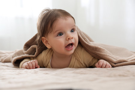 Cute little baby under plaid on bed indoors