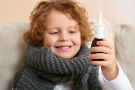 Cute little boy showing nasal spray indoors, focus on bottleの写真素材