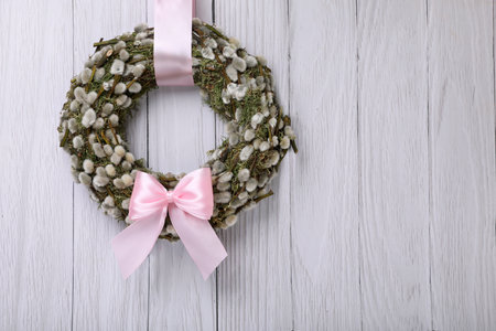 Wreath made of beautiful willow branches and pink bow hanging on white wooden background. Space for textの写真素材