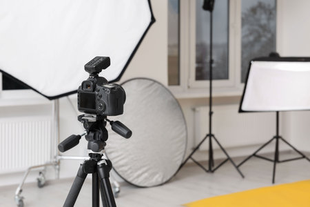 Camera on tripod and professional lighting equipment in modern photo studio, space for textの写真素材