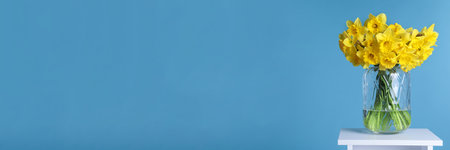 Beautiful daffodils in vase on white table against light blue background, space for text. Banner...