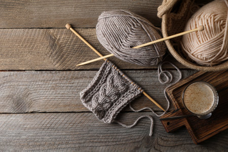 Soft colorful woolen yarn, knitting, needles and glass of coffee on wooden table, flat lay. Space...