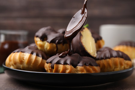 Pouring chocolate cream onto delicious profiterole on table, closeup