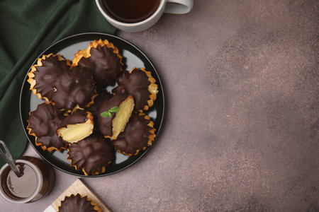 Delicious profiteroles with chocolate spread, cream and aromatic tea on textured table, flat lay....