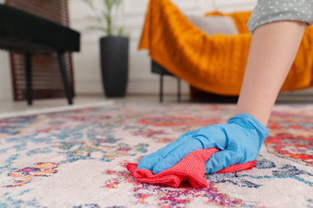 Woman in rubber gloves cleaning carpet with rag indoors, closeup. Space for textの写真素材