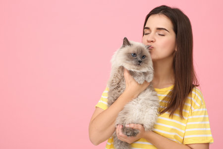 Woman kissing her cute cat on pink background, space for textの写真素材