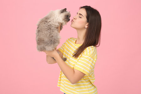 Woman kissing her cute cat on pink backgroundの写真素材