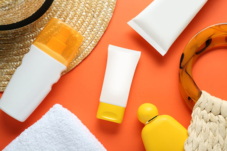 Suntan products, straw hat and bag on orange background, flat lay