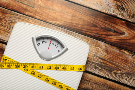 Weigh scales tied with measuring tape on wooden table, top view and space for text. Overweight conceptの写真素材