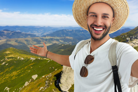 Smiling young man in straw hat taking selfie in mountainsの写真素材