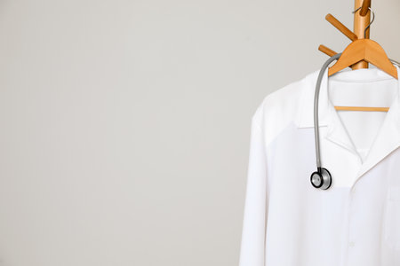 Medical uniform and stethoscope hanging on rack against light gray background. Space for textの写真素材