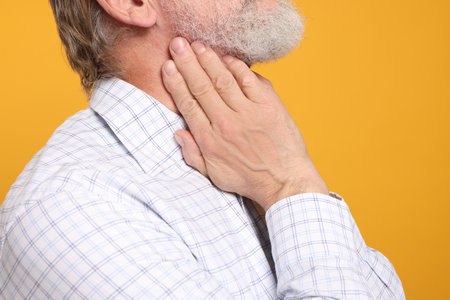 Senior man suffering from sore throat on yellow background, closeup. Cold symptomsの写真素材