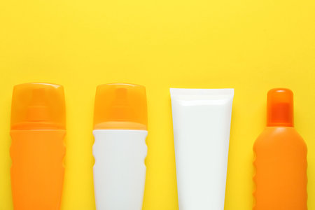 Suntan products on yellow background, flat lay. Space for text