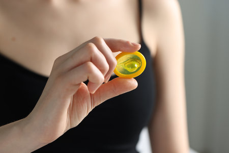 Woman holding unpacked condom on light background, closeup. Safe sexの写真素材