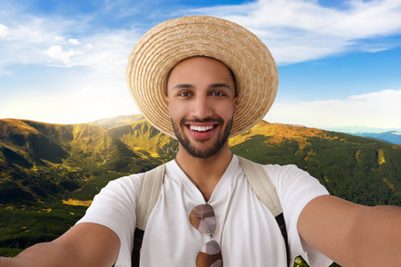 Smiling young man in straw hat taking selfie in mountainsの写真素材