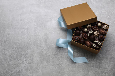 Open box of delicious chocolate candies and color ribbon on light gray table, flat lay. Space for...