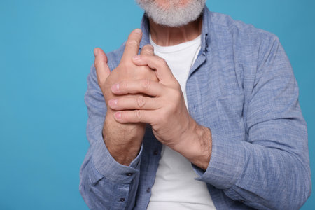 Senior man suffering from pain in hand on light blue, closeup. Arthritis symptomsの写真素材