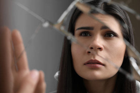 Young woman looking at herself in broken mirror, closeup