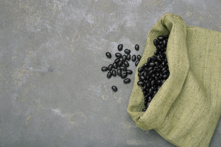 Sack of raw black beans on gray table, top view. Space for text