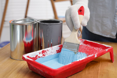 Man taking light blue paint with brush from tray at wooden table indoors, closeupの写真素材