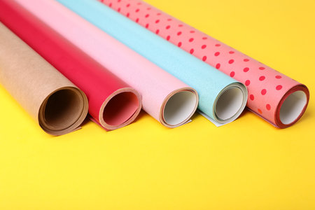 Rolls of colorful wrapping papers on yellow background, closeup
