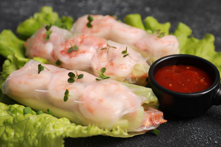Tasty spring rolls served with lettuce, sauce and microgreens on gray textured table, closeup