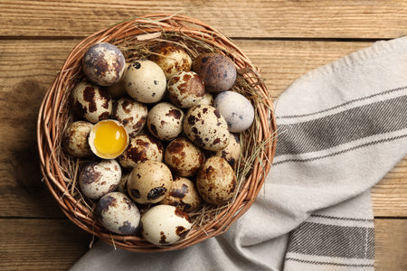 Wicker bowl with quail eggs and straw on wooden table, top viewの写真素材