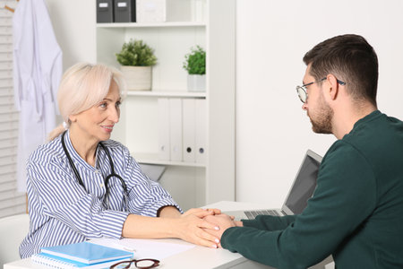 Doctor holding patient's hands at white table during consultation in clinicの写真素材