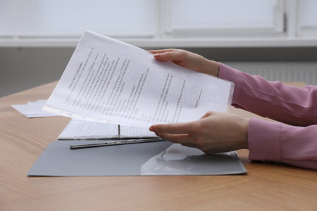 Woman putting punched pocket with document into folder at wooden table, closeupの写真素材