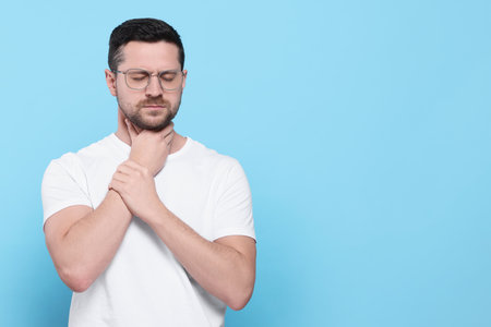 Man suffering from sore throat on light blue background, space for textの写真素材