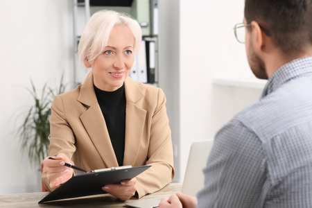 Happy woman with clipboard and man at wooden table in office. Manager conducting job interview with applicantの写真素材