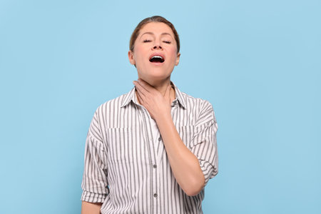 Woman suffering from sore throat on light blue background
