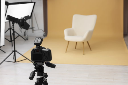 Camera on tripod, armchair and professional lighting equipment in modern photo studio, space for textの写真素材