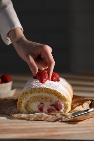Woman decorating delicious cake roll with strawberries at table, closeupの写真素材