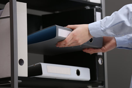 Woman taking folder with documents from shelf in office, closeupの写真素材