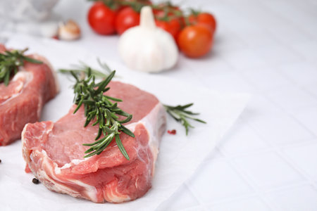 Fresh raw meat with rosemary on white tiled table, closeup. Space for textの写真素材