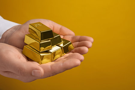 Woman holding many shiny gold bars on yellow background, closeup