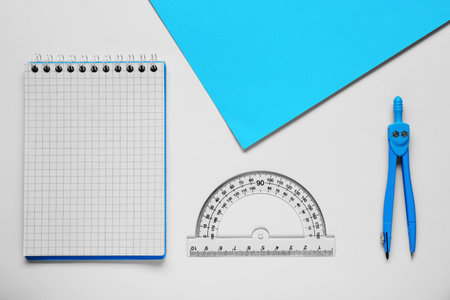 Protractor ruler, paper sheet, notebook and compass on white background, flat lay
