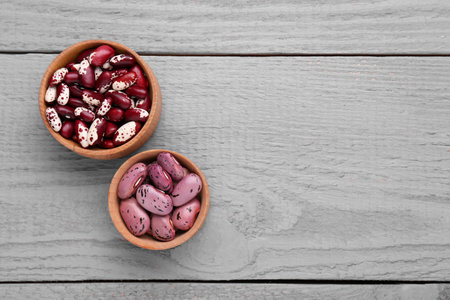 Different kinds of dry kidney beans on gray wooden table, flat lay. Space for text