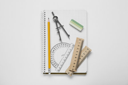 Protractor ruler, compass, pencil and notebook on white background, top view