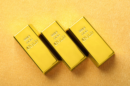 Many shiny gold bars on yellow fabric, flat layの写真素材